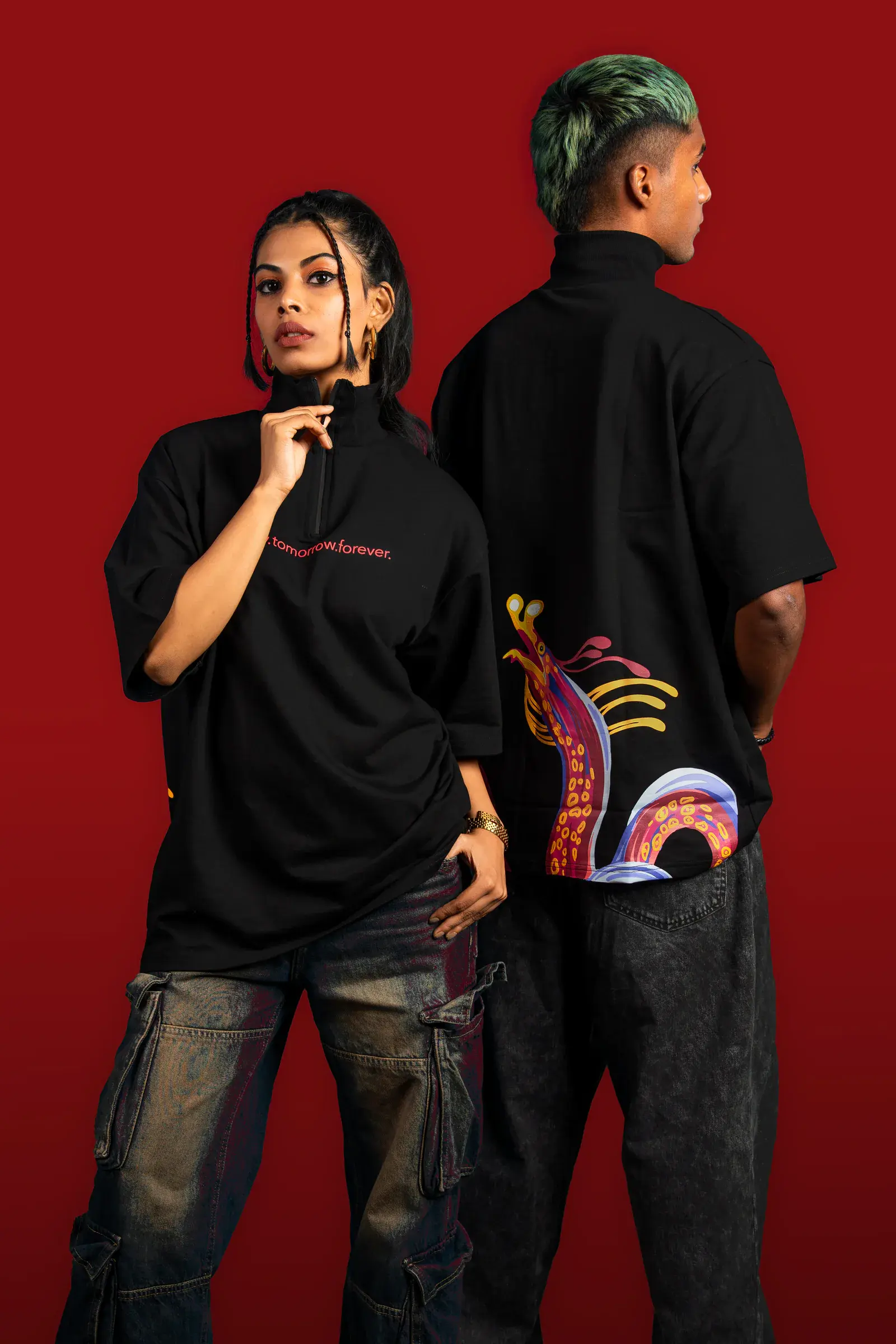 Two models wearing black 224dot graphic streetwear against a deep red studio background