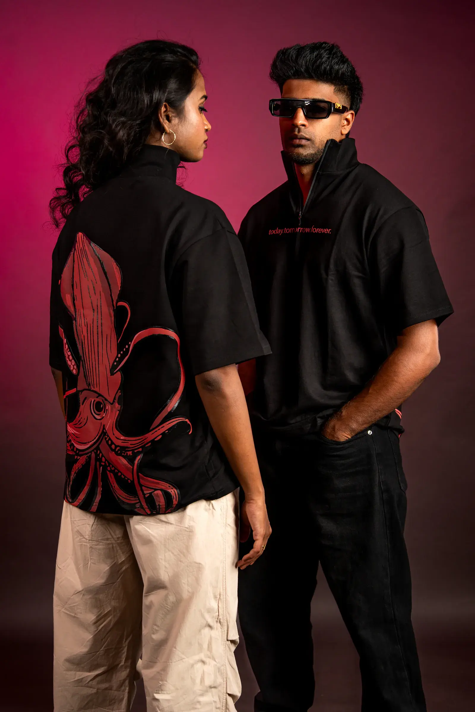 Two models in black 224dot streetwear against a red background